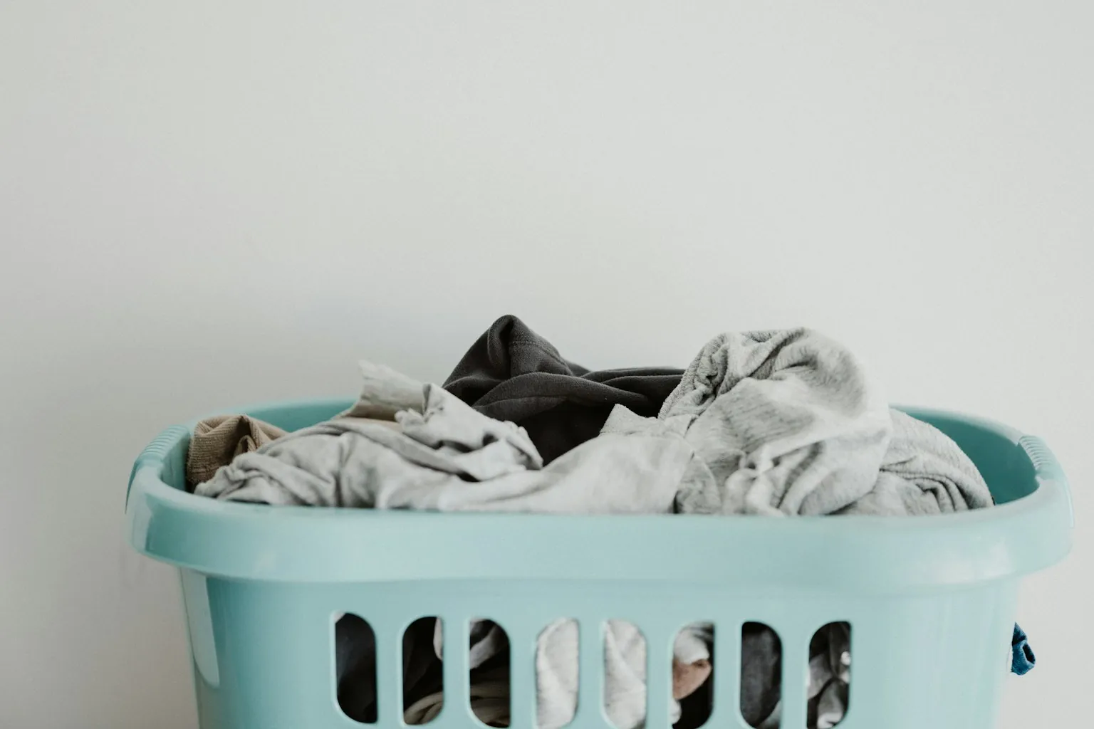 Lichtblauwe wasmand met wasgoed voor een witte muur