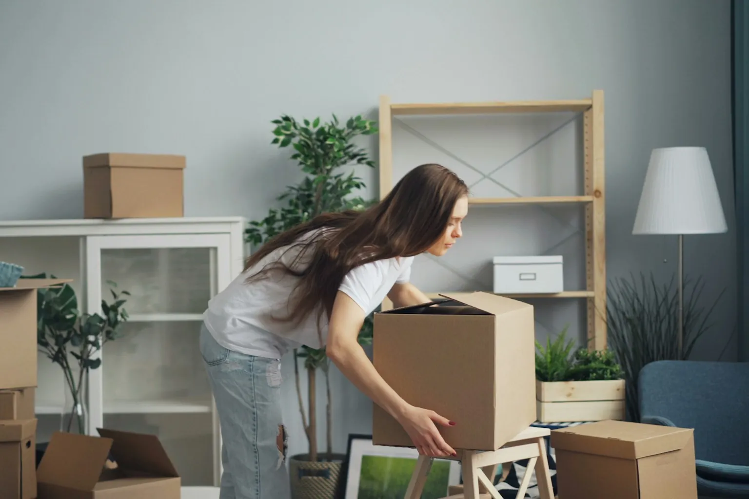 Vrouw tilt een verhuisdoos in een woonkamer vol dozen