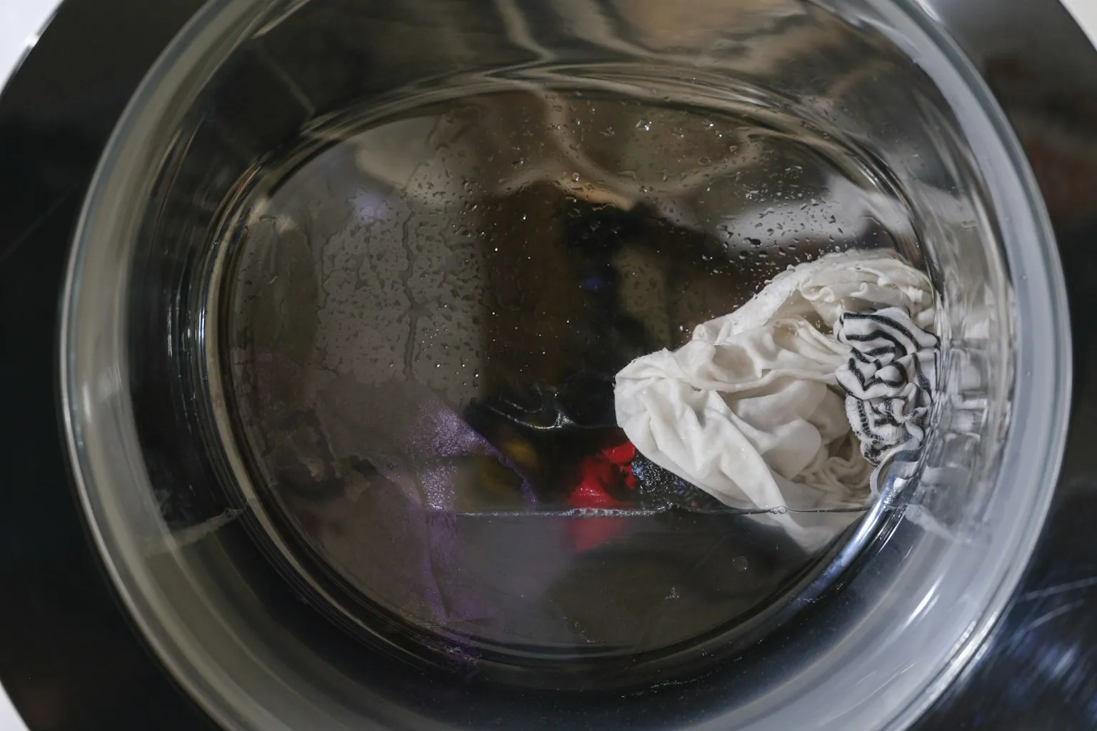 Water en wasgoed achter de deur van een wasmachine die niet heeft afgepompt